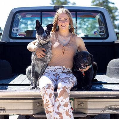 Young adult female sitting in the bed of a pickup truck with a dog on each side