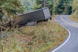 Semi trailer spanning a creek bed with a curved road to the right of the image.