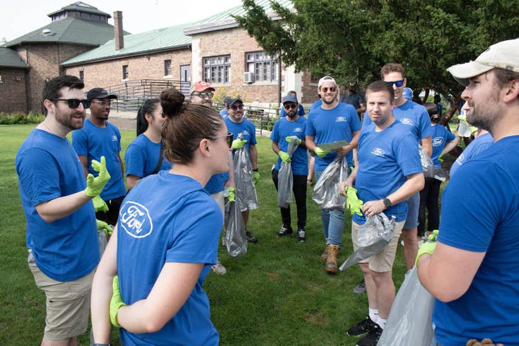 More than a dozen people wearing blue Ford Volunteer T-shirts, standing outside the back of the Belle Isle Casino building, listening to cleanup instructions.