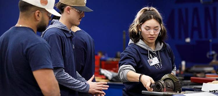 Two male students look on as a female student handles an engine rotor