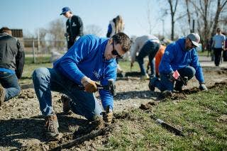 Two males edging the walkway with others working in the background