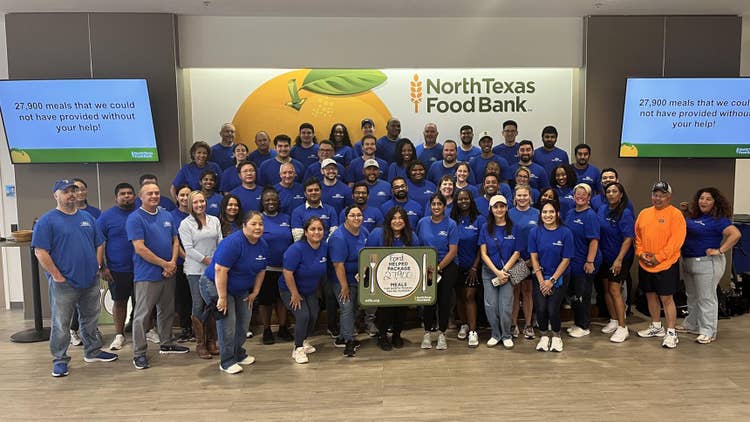North Texas Food Bank banner on the wall behind almost 50 people in Ford Volunteer T-shirts with a sign in front with Ford Helped package 27,900 meals for North Texans Facing Hunger with ntfb.org and North Texas Food Bank in each bottom corner.