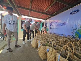 Five persons under an awning in line near rows of baskets in front of a Global Caring Month banner.