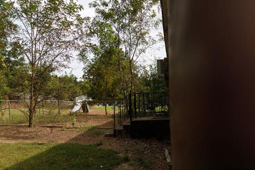 Back portion of Stanton School showing window air conditioner, steps leading to a yard with a metal slide and bordered by a metal chain link fence.