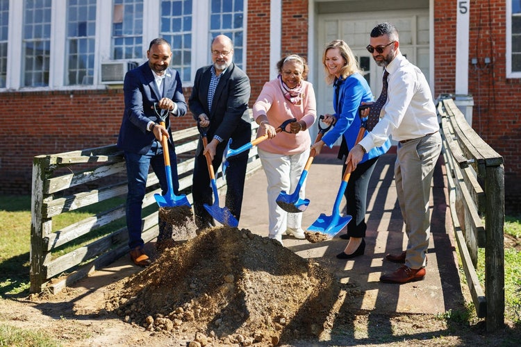 Five persons including Dr. Clarice White, project champion and Stanton School alumna, Hassan Hammoud, Senior Manager of Essential Services for Ford Philanthropy, Mary Culler, President of Ford Philanthropy, adding dirt to a pile with shovels at the base of a ramp leading to Stanton School.