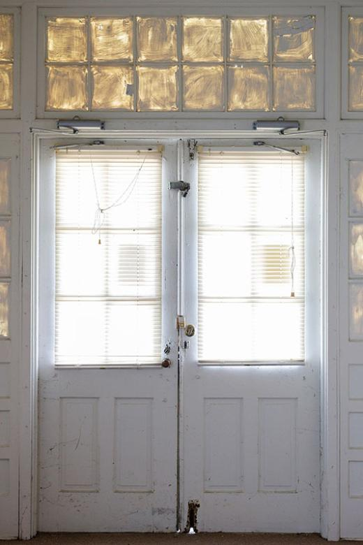 Interior view of white double doors that lead outside. Windows above doors painted white.