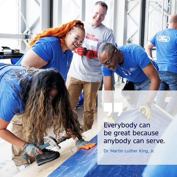 Three people in blue Ford Volunteer T-shirts and one person in a Team Rubicon shirt working and watching a tarp attachment to wood. Others are in the background working on different projects. Text in a gray box in the lower right corner: Everybody can be great because anybody can serve. Dr. Martin Luther King, Jr.