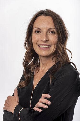 Ana Eseverri Mayer headshot, female with slightly curled long brown hair, black blouse with gold trim at V-neck line