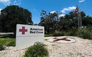Red Cross sign in the front of the office building with a red cross in a circle of stone separated from the gravel by a ring, with flags in the background.