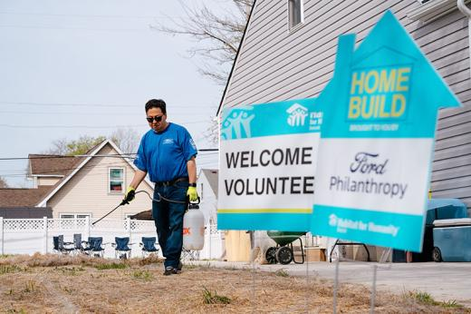 Male outside watering lawn with Habitat for Humanity WELCOME VOLUNTEERS and HOME BUILD Ford Philanthropy signs in the foreground