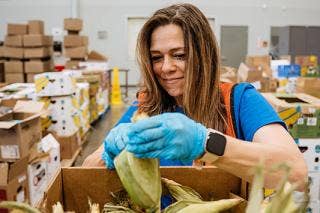 Gloved female in a warehouse holds ear of corn, preparing to remove husks.