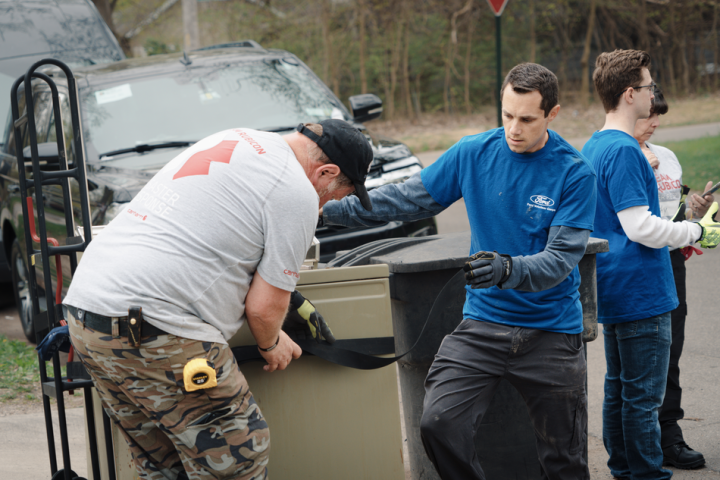Ford blue shirt volunteers using a dolly to haul a freezer