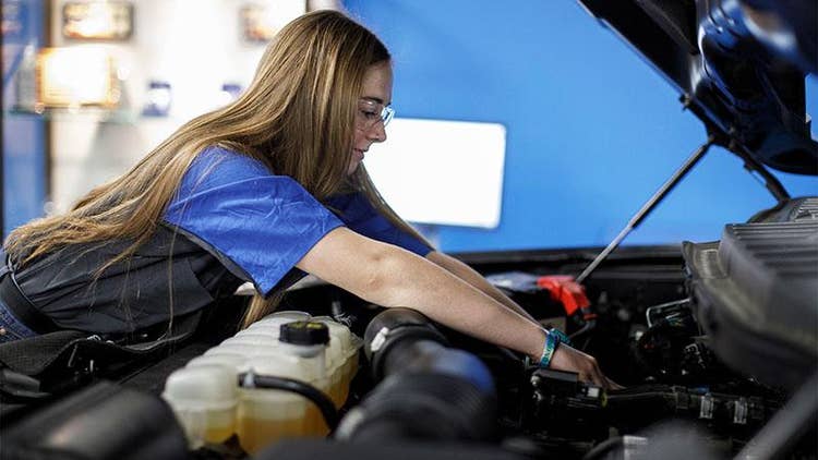 Female wearing safety goggles working under the hood and working on a vehicle engine.