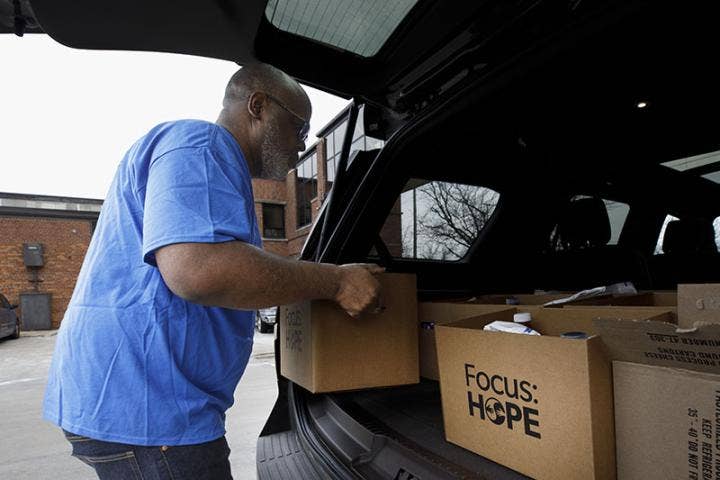 African American male lifting a cardboard box labeled Focus: HOPE just outside back of vehicle with like labeled boxes