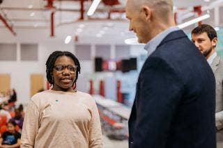African American female student wearing glasses with two adult males in a classroom.