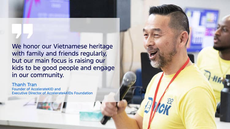 Text: We honor our Vietnamese heritage with family and friends regularly, but our main focus is raising our kids to be good people and engage in our community. Thanh Tran Founder of AccelerateKID and Executive Director of Accelerate4KIDs Foundation to left of Asian male wearing a light yellow T-shirt with '22 D HACK on the front. He holds a microphone in his right hand standing in front of a receptionists counter with an African American male behind.