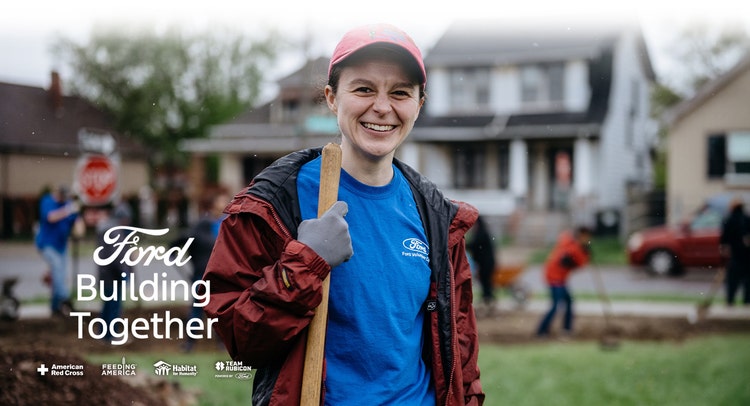 Blue shirt Ford volunteer holding a shovel smiling