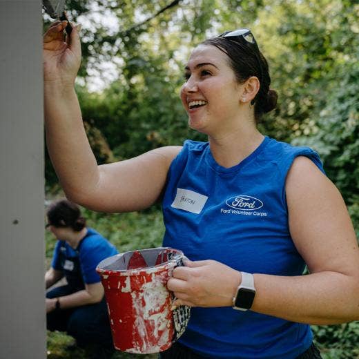 Woman in Ford Blue oval volunteer shirt holding a paintbrush