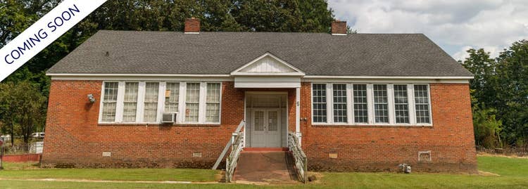 Wide red brick building sitting on green grass featuring many front tall windows